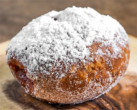 Plain beignets covered in powdered sugar on a wood board.
