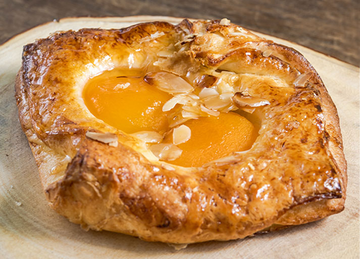 Image of a golden, flaky Danish pastry filled with sweet peaches or blueberries.