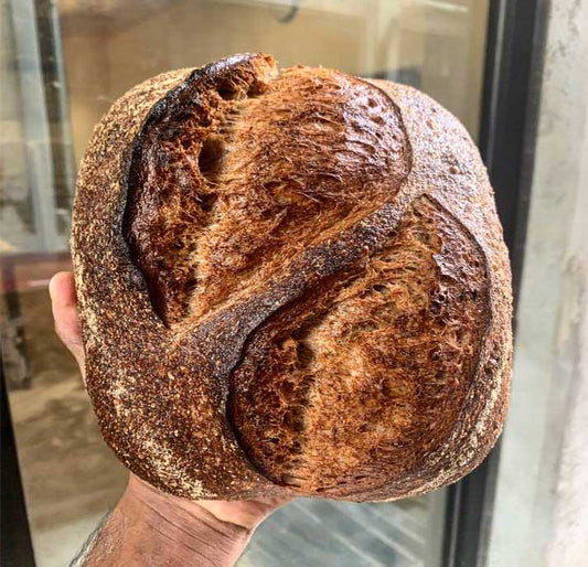 Image of a dark rye sourdough loaf on a wood slab, made with a blend of rye flour and sourdough starter for a unique, tangy flavor. Dense and flavorful, this bread is perfect for sandwiches, toast, or as a side to any meal.